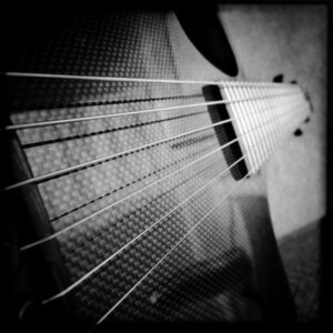 Square black and white image of a black guitar, looking up at it from an angle